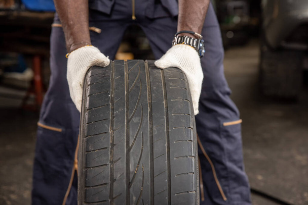A tire at the repair garage. mechanic hands pushing a black tire in the workshop. - Photo, image