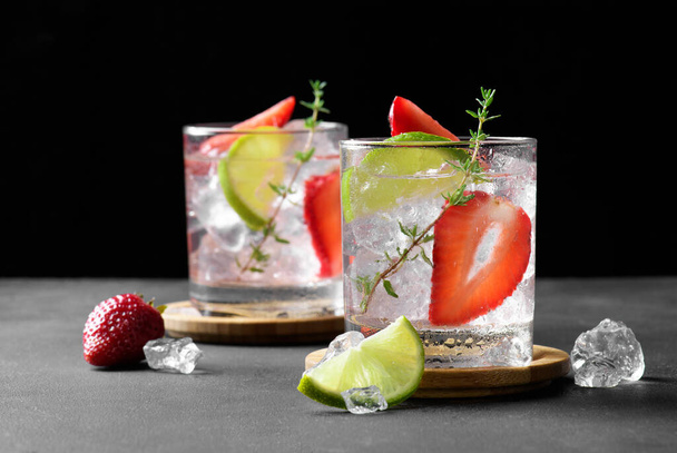 Fresh strawberry mojito cocktail. Two glasses with cold summer strawberry soda drink with strawberry, ice cubes and lime, decorated wiht thyme on dark background. Iced strawberry lemonade, close up - Photo, image