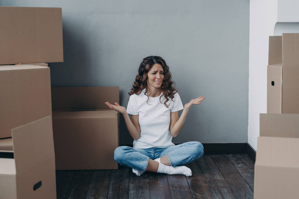 Nervous european woman has to pack the boxes. Girl is upset with moving. Annoyed young lady in jeans and white t-shirt is going to relocate. Homeowner getting stress from moving concept. - Zdjęcie, obraz