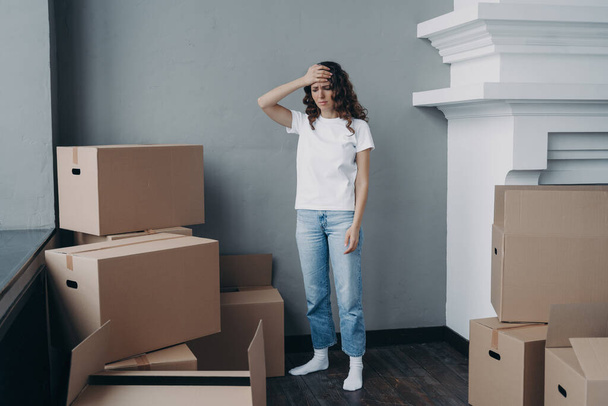Tired girl is moving. Woman getting headache from boxes packing. Annoyed young lady in jeans and white t-shirt is going to relocate. Homeowner gathering things and getting away from luxurious house. - Foto, immagini