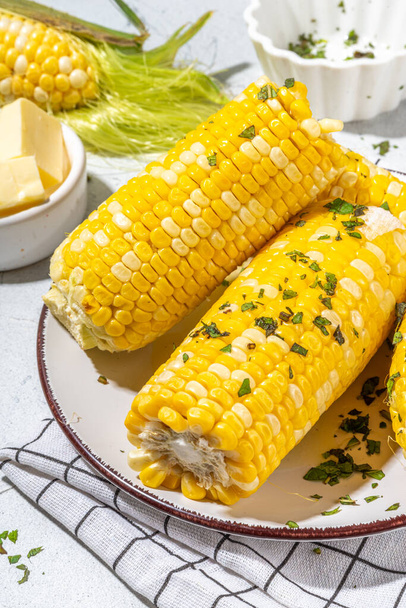 Boiled corn with butter and herbs. Ripe yellow organic cooked corn cobs, on a white kitchen table - Foto, afbeelding