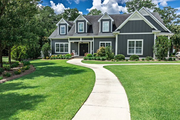 A large gray craftsman new construction house with a landscaped yard and a long leading walkway to the front door. - Zdjęcie, obraz