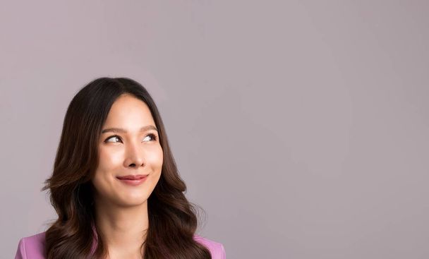 Asian woman long hair, wearing a pink suit is smiling and looking at the gray empty background. - Foto, imagen