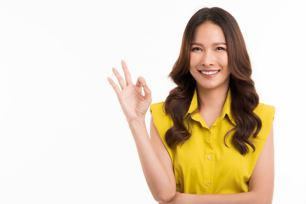 Happy Asian woman wearing a green shirt shows the ok sign and looks at the camera on white background. - Foto, Imagem