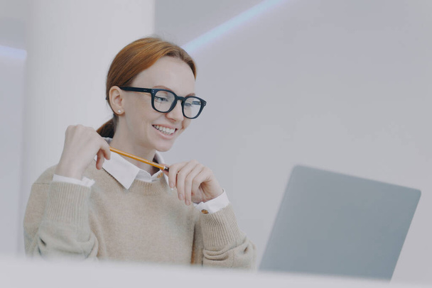 Young european businesswoman in glasses is happy. Secretary or manager at workplace in modern office. Successful attractive girl is studying at laptop. Positive female student. - Zdjęcie, obraz