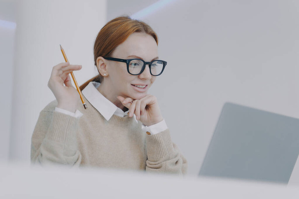 Female student is reading on PC. Smiling girl is browsing information and doing research. Adviser or manager at workplace in modern office. Successful attractive girl is studying. - 写真・画像