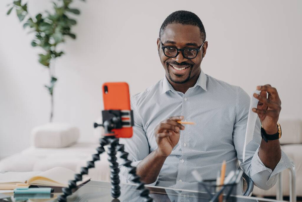 African american businessman presenting financial statistics by business corporate video call, using phone. Smiling friendly black male business coach teaching distantly online, showing document. - Valokuva, kuva