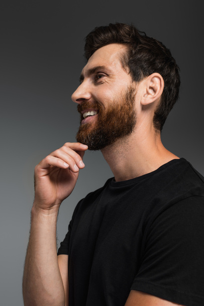 portrait of happy man with beard in black t-shirt smiling isolated on grey - Zdjęcie, obraz