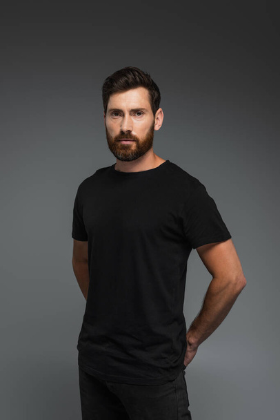 portrait of good-looking man in black t-shirt looking at camera isolated on grey - Foto, Bild
