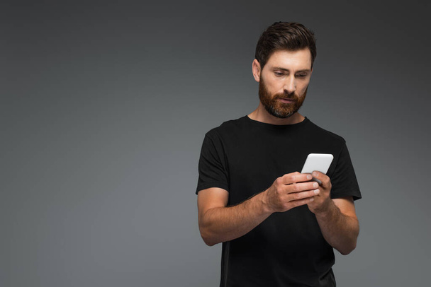 bearded man in black t-shirt using smartphone isolated on grey - Photo, image