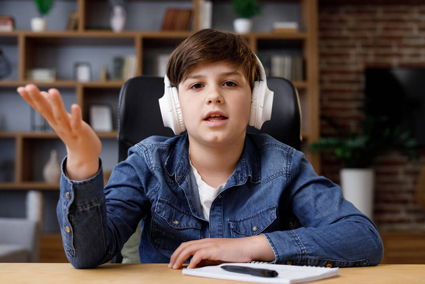 Portrait of schoolboy wearing earphones has online lesson,video call with teacher,answering questions, check of knowledge. Cute teenager studying at home using laptop. Distance learning. Web cam view - Фото, зображення