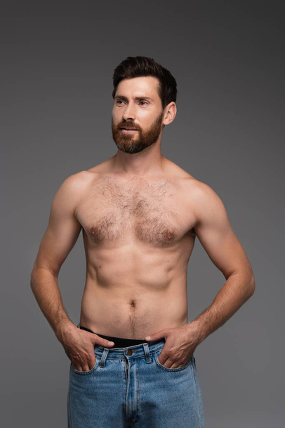 shirtless and bearded man with hair on chest posing with hands in pockets isolated on grey - Foto, Imagem