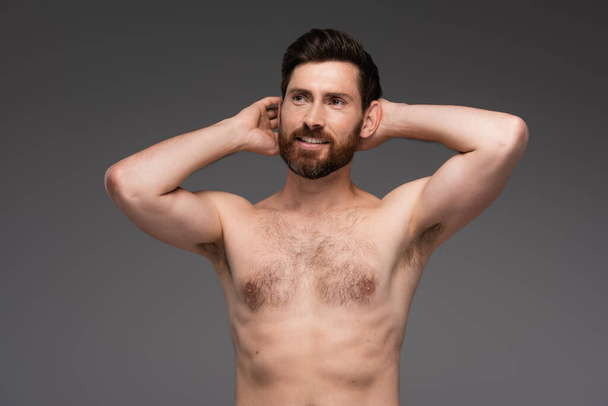 shirtless and happy man with hair on chest posing with hands behind head isolated on grey - 写真・画像