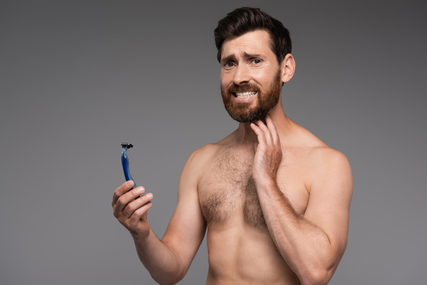 displeased and shirtless man with beard holding safety razor isolated on grey - Foto, immagini