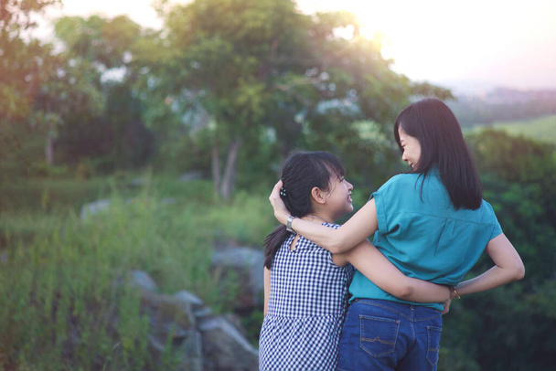 Мать и дочь обнимаются и веселятся на свежем воздухе в зеленой природе с закатом. - Фото, изображение