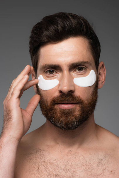 portrait of bearded man with moisturizing eye patches isolated on grey  - Fotó, kép