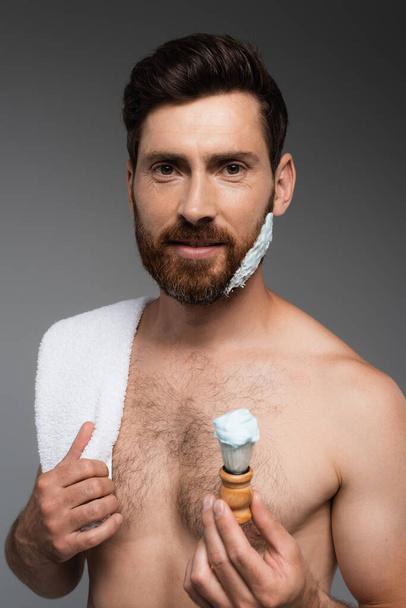 bearded man with shaving foam on face holding shaving brush isolated on grey - Foto, imagen