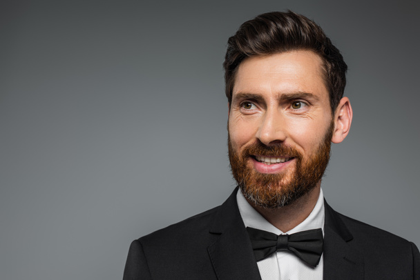 cheerful and bearded man in black tuxedo with bow tie isolated on grey - Foto, Imagem