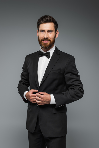 bearded man in black tuxedo with bow tie smiling isolated on grey - Foto, Imagem