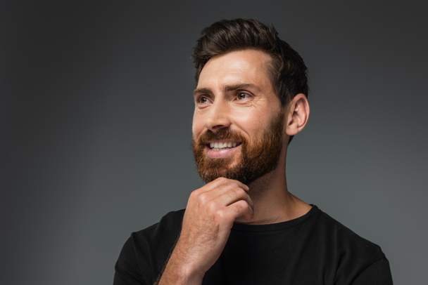 portrait of cheerful man touching beard and looking away isolated on grey - Fotografie, Obrázek