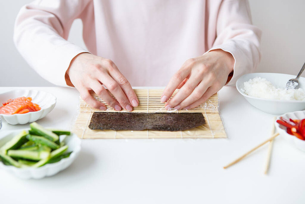 Διαδικασία παρασκευής σούσι, το κορίτσι κάνει σούσι με διαφορετικές γεύσεις - φρέσκος σολομός, χαβιάρι, αβοκάντο, αγγούρι, τζίντζερ, ρύζι - Φωτογραφία, εικόνα