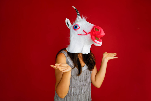 a surprised woman in a unicorn mask on a red background with copy space.  - Zdjęcie, obraz