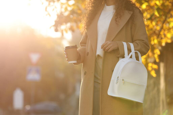 African-American woman with stylish white backpack and hot drink outdoors on sunny day, closeup. Space for text - Foto, Imagen
