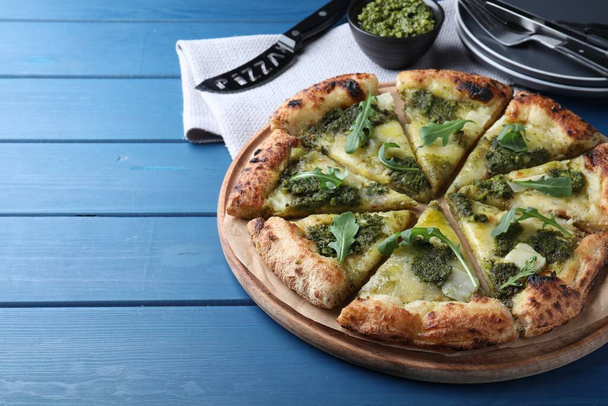 Delicious pizza with pesto, cheese and arugula on blue wooden table. Space for text - Foto, Imagem
