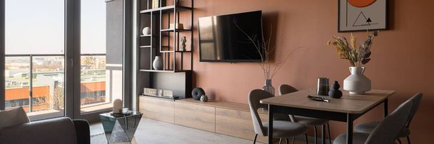 Panorama of modern tv room with orange wall, big window and dining table - Фото, изображение