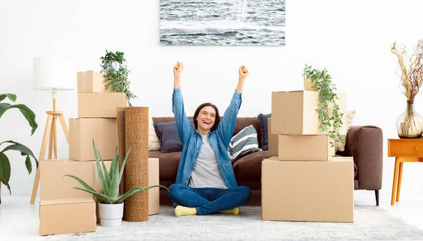 Happy smiling Caucasian woman sitting on the floor in her new flat with a stack of cardboard boxes. Moving to a new house, rent - Foto, immagini