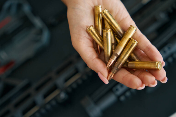 Shiny live ammunition on a delicate female palm against the background of a modern machine gun - 写真・画像