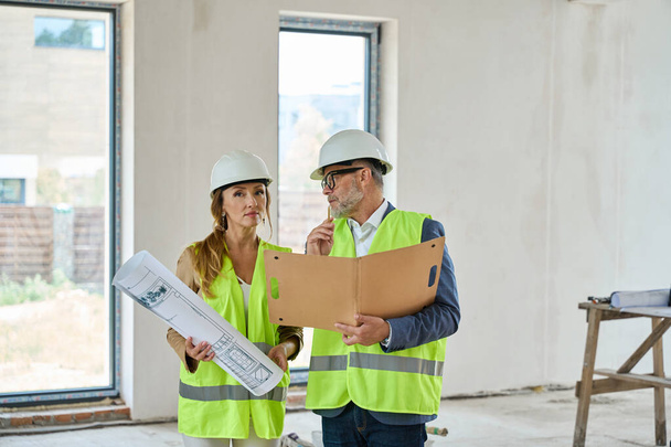 Real estate agent with blueprints and a foreman with folders in their hands are talking while standing in an unfinished house - Photo, image