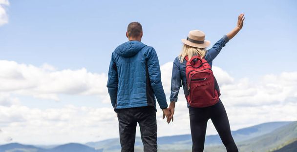 Rear view of hiking couple with backpack standing together on hill top enjoying beautiful landscape. Man and woman outdoors on hiking standing on a rock. - Fotó, kép