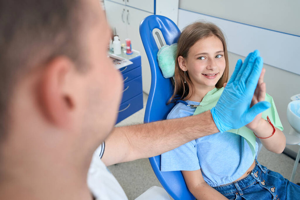Smiling pleased teenage girl giving her pedodontist high five after successful teeth treatment - Fotó, kép