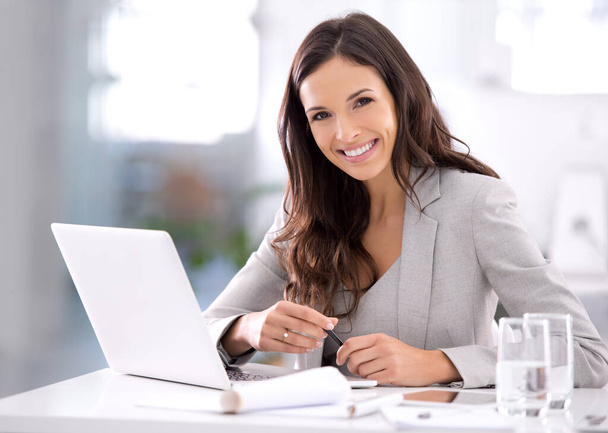 Happy, confident and ambitious business woman working on her laptop while sitting at her desk. Portrait of a beautiful female entrepreneur showing great leadership skills while working in an office. - Foto, Bild