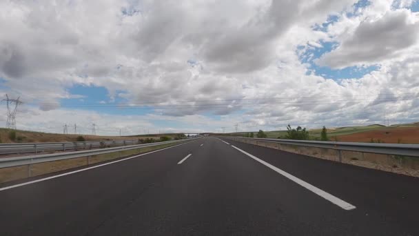 POV driving a car on empty highway road through the fields outside the city during sunny day. Two way asphalt road country views with low clouds at Spain. Traffic ways transportation concept. - Video