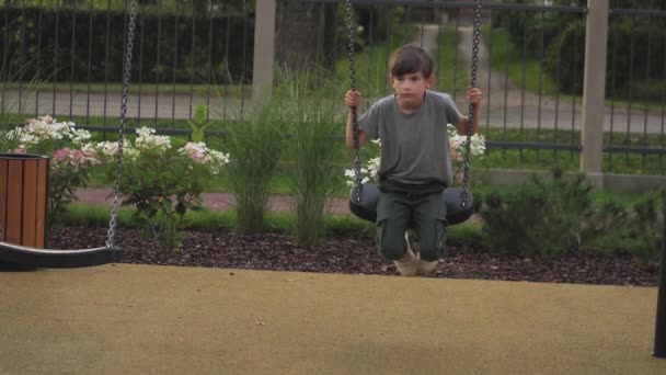 A little boy was swinging on a swing. Playground with one child. The boy rested on the swing - Materiał filmowy, wideo