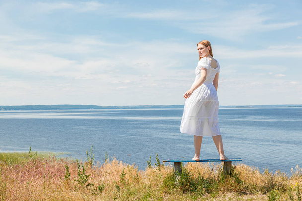 Krásná dívka stojí na lavičkách na pobřeží s výhledem na oblohu zblízka - Fotografie, Obrázek