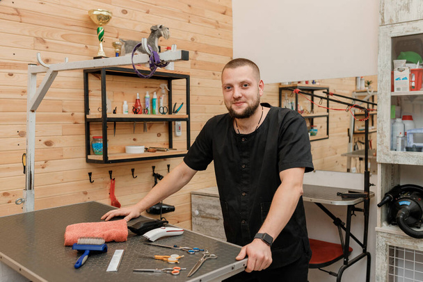 Handsome male groomer with professional equipment on his workplace in grooming salon for pet - Фото, зображення