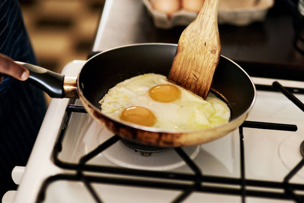 Яйца всегда готовят хороший завтрак. Неузнаваемый человек, жарящий яйца, пока готовит завтрак на кухне дома - Фото, изображение