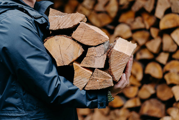 Close up of unrecognizable man dressed in jacket carries bundle of firewood, going to make fire outdoor. Winter is coming. - Photo, Image