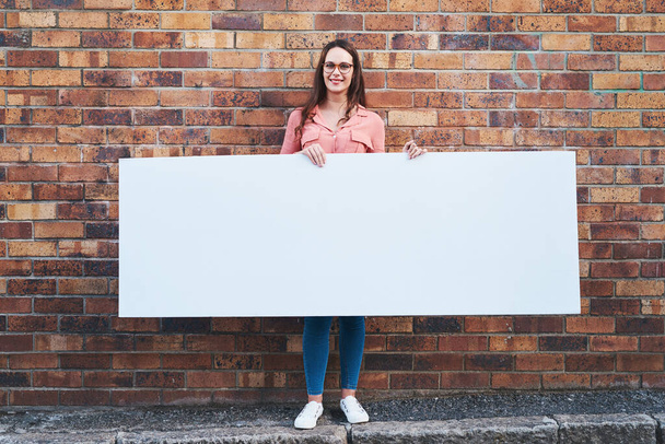 Η σήμανση δεν γίνεται μεγαλύτερη από αυτό. μια νεαρή γυναίκα που κρατά ένα λευκό πανό σε αστικό φόντο σε εξωτερικούς χώρους - Φωτογραφία, εικόνα