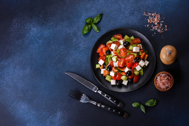 Свіжий грецький салат з помідорами, огірком, перцем, оливками та сиром фета на чорній тарілці
 - Фото, зображення