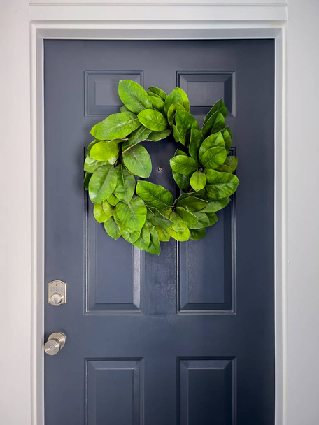 Front view of a navy blue door with a colorful green wreath on a bright, sunny day - Photo, image