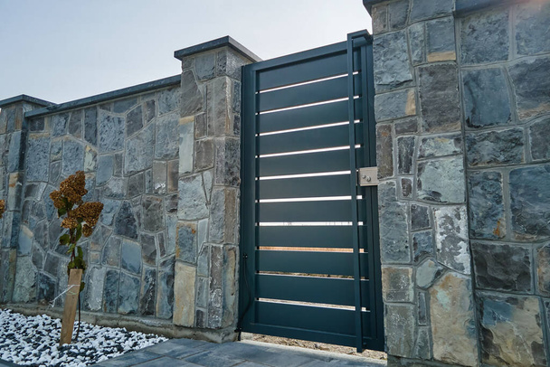 Stone high fence with shut iron door in paved yard of modern style design property outdoor. - Photo, Image