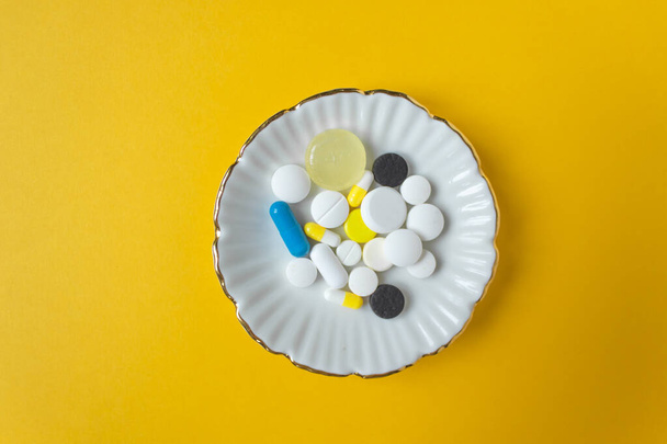 Round plate with different multicolored pills, capsules and drops. Yellow background. Tablets are ready to eat instead of food. Top view. Horizontal photo and space for text. - Photo, image