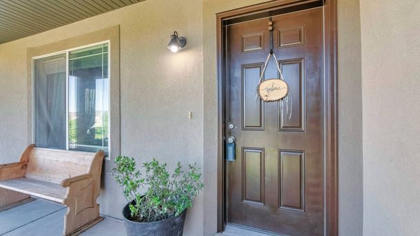 Panorama Brown front door with lockbox and hanging welcome signboard. Entrance of a house with potted plants and wooden bench near the window. - Foto, immagini