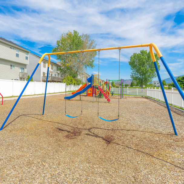 Square Whispy white clouds Small community playground near the fenced residential houses at Utah Valley. There are colorful playground equipments inside the picket fence - 写真・画像