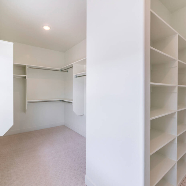 Square Master closet interior with window and carpeted flooring. There are divider shelves at the front and wall mounted shelves with metal rods at the back. - 写真・画像