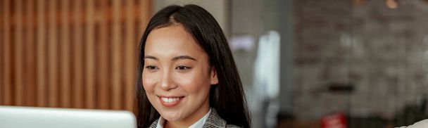 Primer plano de la sonriente mujer de negocios asiática trabajando portátil sentado en acogedora oficina. Foto de alta calidad - Foto, imagen